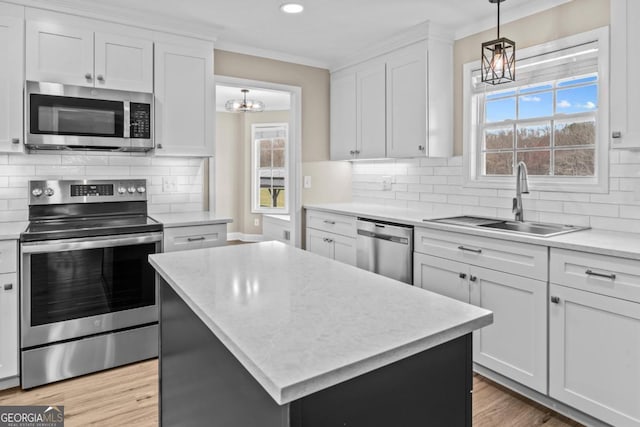 kitchen with light wood finished floors, stainless steel appliances, decorative backsplash, ornamental molding, and a sink