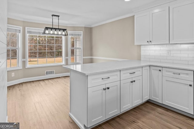 kitchen featuring visible vents, ornamental molding, white cabinets, wood finished floors, and a peninsula