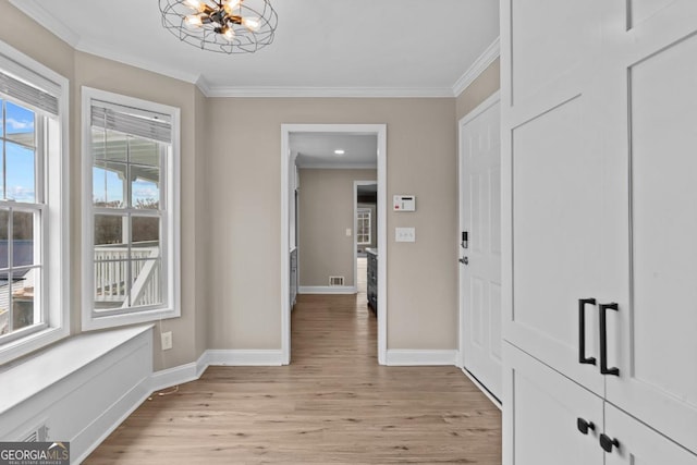 hallway with visible vents, baseboards, light wood-style flooring, crown molding, and a notable chandelier