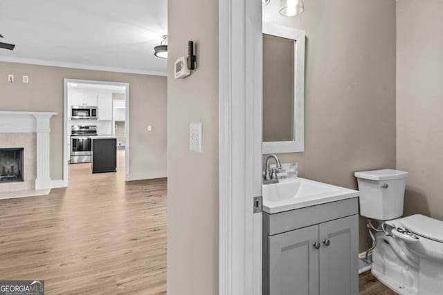 bathroom featuring toilet, a premium fireplace, wood finished floors, vanity, and crown molding