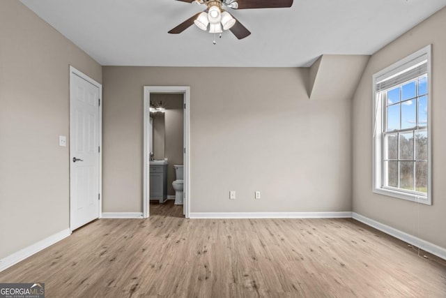 unfurnished bedroom featuring a ceiling fan, ensuite bathroom, baseboards, and wood finished floors