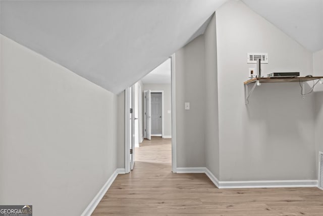 corridor with lofted ceiling, light wood-type flooring, visible vents, and baseboards