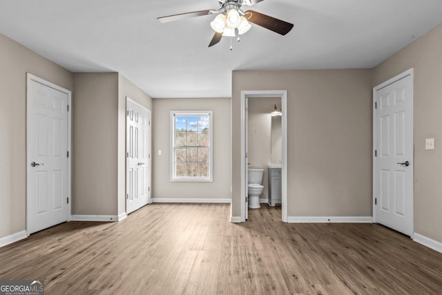 unfurnished bedroom featuring ensuite bathroom, wood finished floors, a ceiling fan, and baseboards