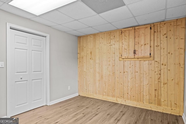 spare room with a paneled ceiling, wood walls, baseboards, and wood finished floors