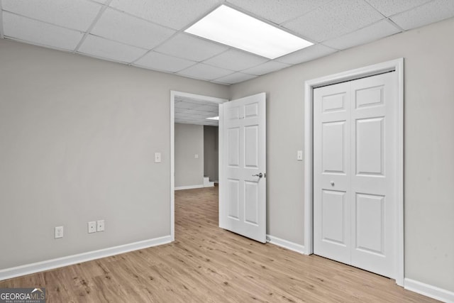 unfurnished bedroom with light wood finished floors, a closet, a paneled ceiling, and baseboards