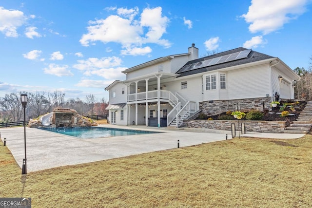 rear view of property featuring a yard, roof mounted solar panels, a patio, and stairway