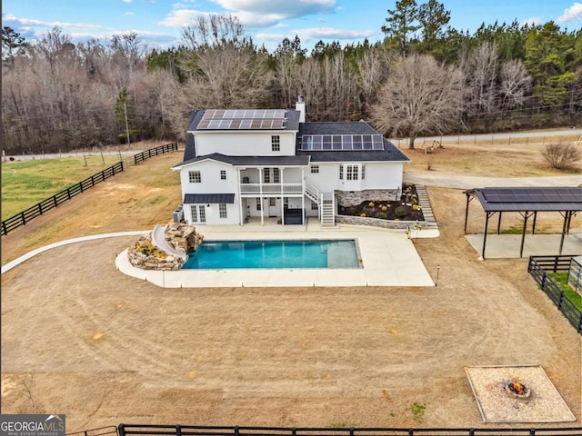 back of property featuring a fire pit, a fenced in pool, fence private yard, a patio area, and roof mounted solar panels