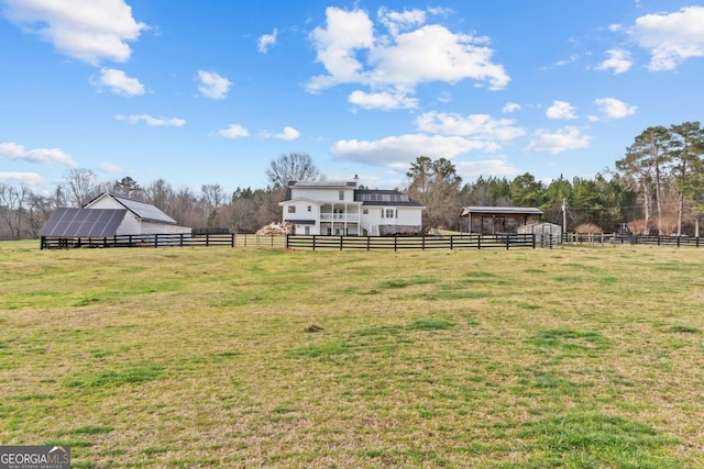 view of yard with fence, an outdoor structure, and a rural view