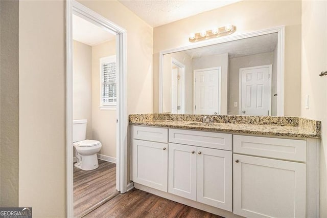 bathroom with toilet, a textured ceiling, vanity, wood finished floors, and baseboards