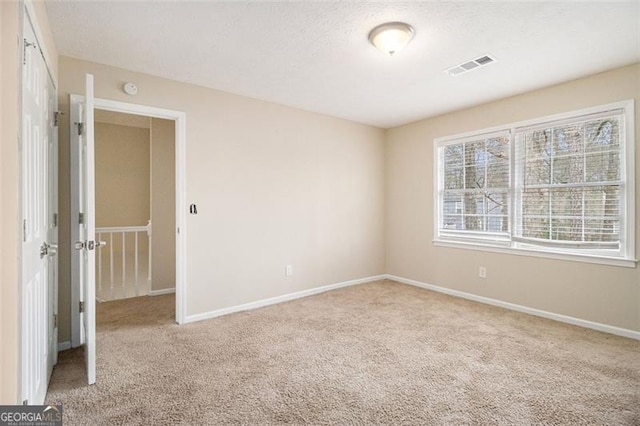 empty room featuring carpet, a textured ceiling, visible vents, and baseboards