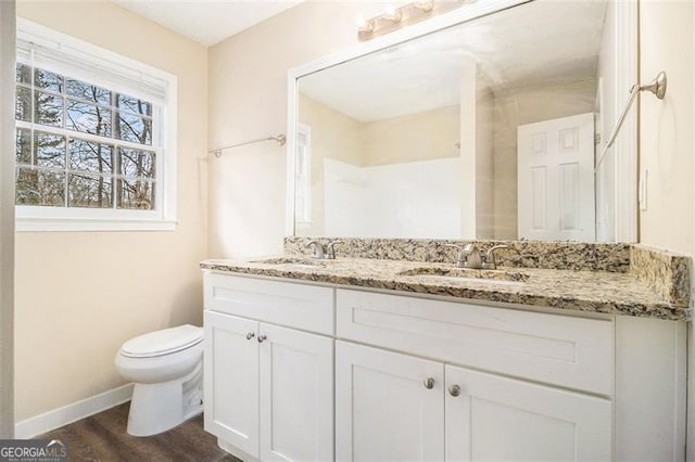 bathroom featuring toilet, double vanity, baseboards, and a sink