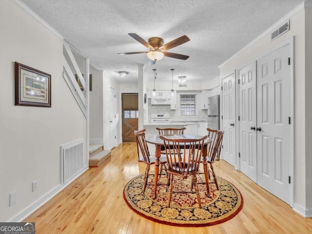 dining room with ornamental molding, light wood-type flooring, and visible vents