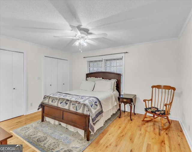 bedroom with a textured ceiling, light wood-style flooring, baseboards, two closets, and crown molding