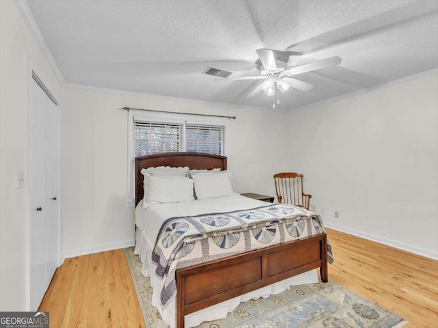 bedroom featuring a textured ceiling, ornamental molding, wood finished floors, and visible vents