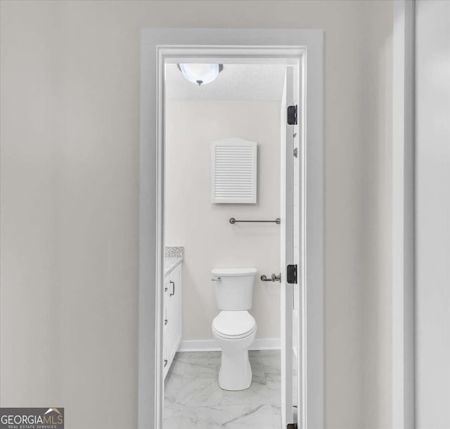 bathroom with marble finish floor, toilet, a textured ceiling, vanity, and baseboards