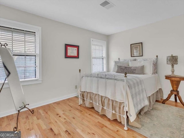 bedroom featuring baseboards, multiple windows, visible vents, and wood finished floors