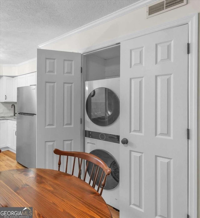 interior space featuring a textured ceiling, ornamental molding, visible vents, and stacked washer / drying machine