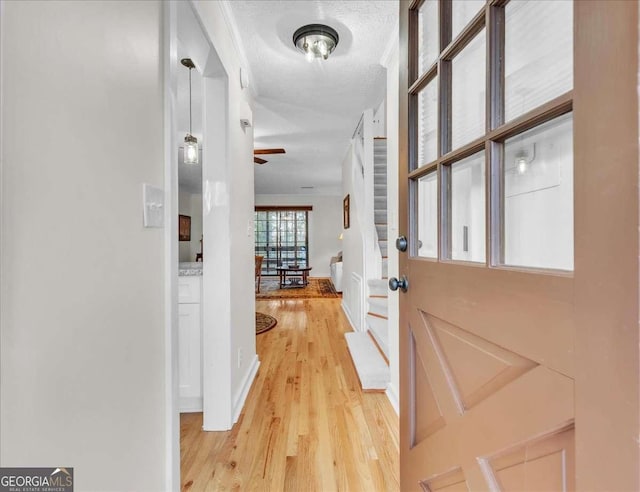 hall with light wood-type flooring, baseboards, and a textured ceiling