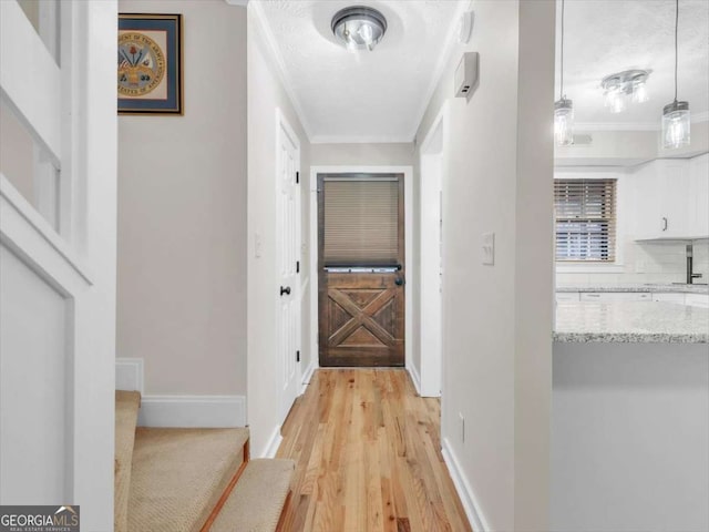 corridor featuring light wood-style floors, crown molding, stairway, and baseboards