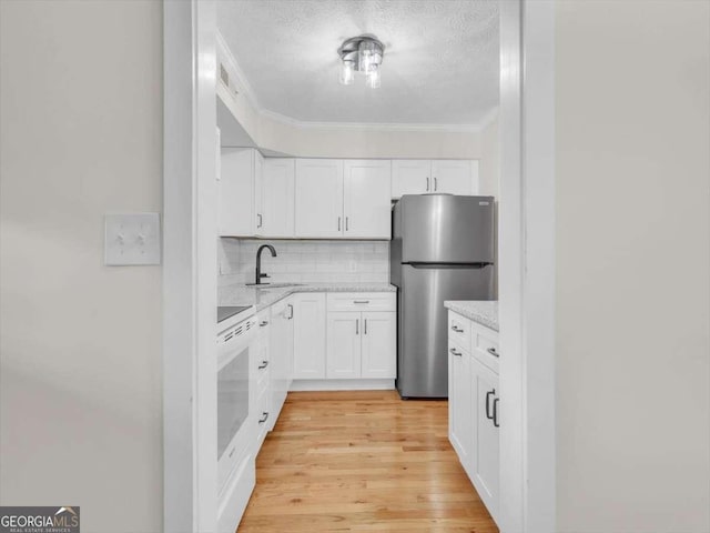 kitchen with decorative backsplash, stove, freestanding refrigerator, white cabinetry, and a sink