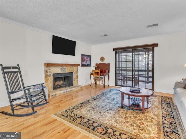 living room with crown molding, a fireplace, visible vents, and wood finished floors