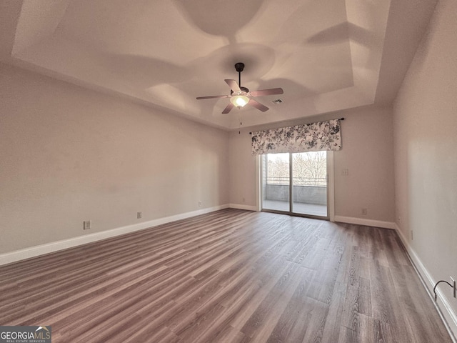 spare room with a tray ceiling, visible vents, ceiling fan, wood finished floors, and baseboards