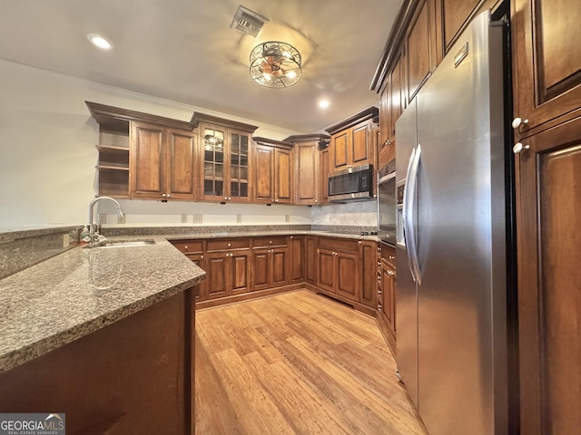 kitchen featuring open shelves, stainless steel appliances, glass insert cabinets, a sink, and light wood-type flooring