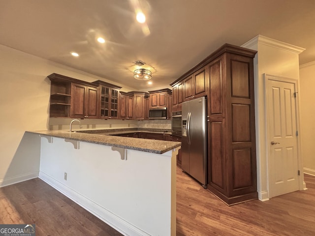 kitchen with a breakfast bar, open shelves, appliances with stainless steel finishes, wood finished floors, and a peninsula