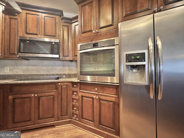 kitchen with light wood finished floors, stone counters, appliances with stainless steel finishes, and decorative backsplash