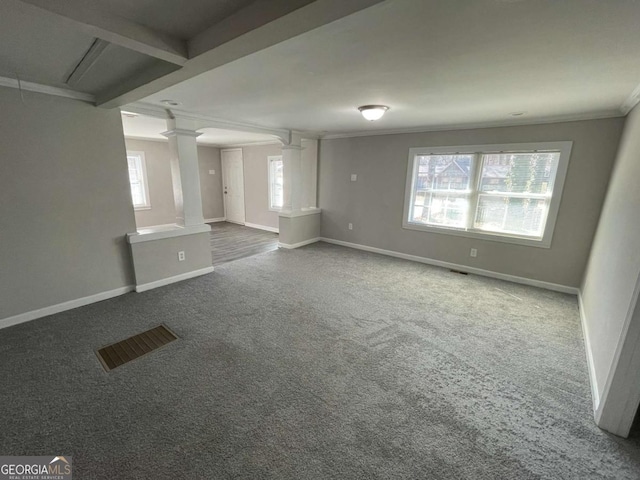 unfurnished living room with decorative columns, attic access, baseboards, ornamental molding, and dark colored carpet