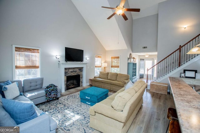 living area with a fireplace, visible vents, a ceiling fan, wood finished floors, and stairs