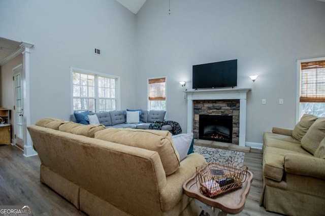 living room with a fireplace, visible vents, wood finished floors, high vaulted ceiling, and baseboards