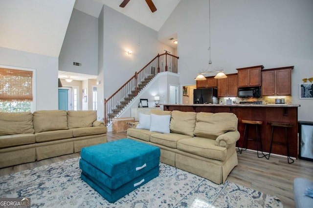 living room featuring visible vents, a ceiling fan, a high ceiling, stairs, and light wood-style floors