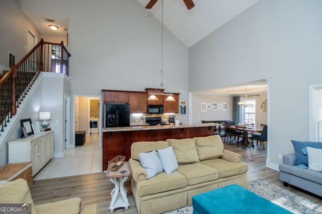 living room featuring light wood finished floors, stairs, baseboards, and ceiling fan with notable chandelier