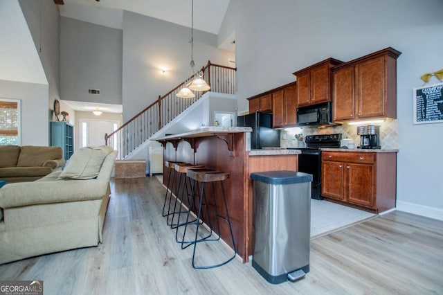 kitchen featuring a breakfast bar, open floor plan, light wood-type flooring, backsplash, and black appliances