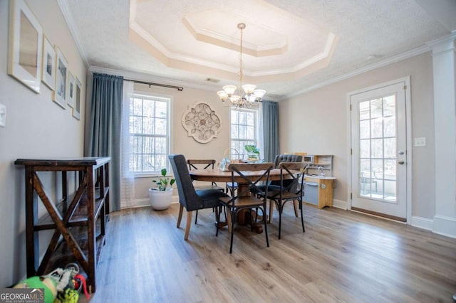 dining area with light wood-style flooring, a tray ceiling, and crown molding