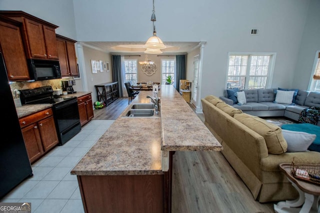 kitchen featuring visible vents, a towering ceiling, open floor plan, black appliances, and a sink