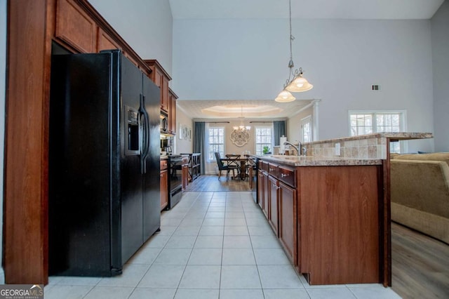 kitchen featuring a center island with sink, hanging light fixtures, light tile patterned flooring, a sink, and black appliances