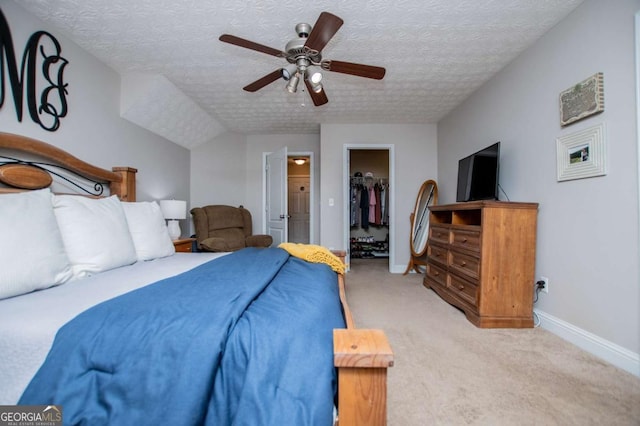 bedroom featuring a spacious closet, light carpet, ceiling fan, a textured ceiling, and baseboards