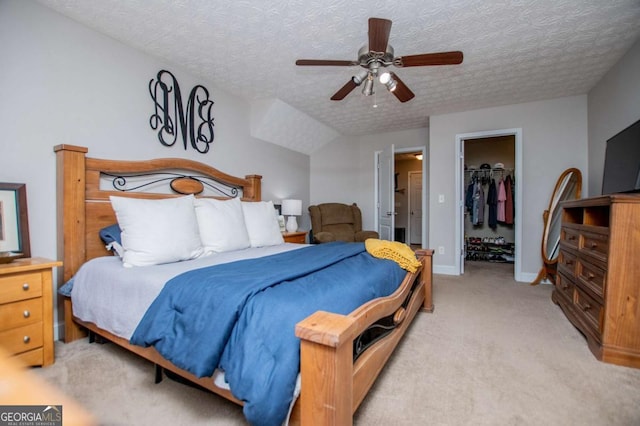 bedroom featuring a textured ceiling, ceiling fan, light colored carpet, a closet, and a walk in closet