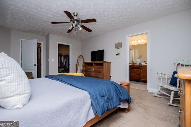 carpeted bedroom with a textured ceiling, ceiling fan, ensuite bathroom, a closet, and a walk in closet