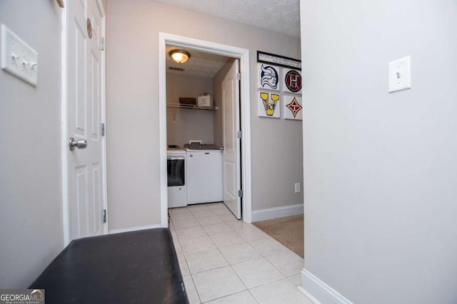 hall featuring baseboards, washer and clothes dryer, a textured ceiling, and light tile patterned flooring