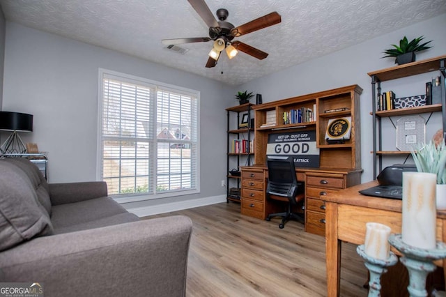 home office featuring a textured ceiling, ceiling fan, visible vents, baseboards, and light wood-type flooring