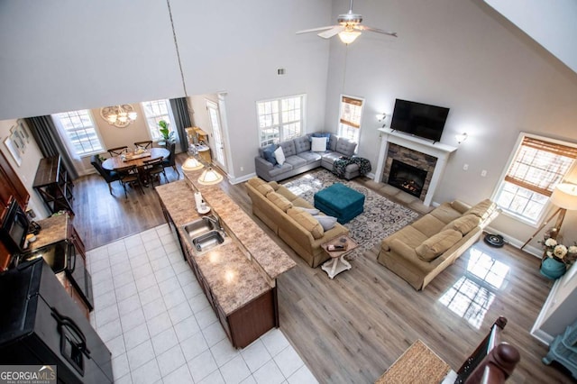 living area with baseboards, a fireplace, light tile patterned flooring, and ceiling fan with notable chandelier