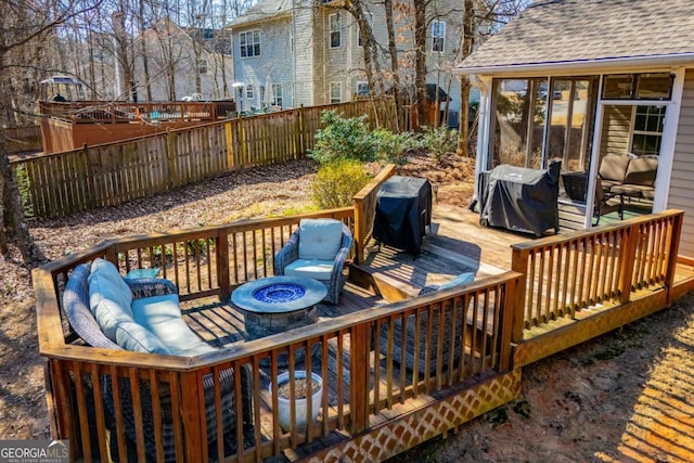 wooden deck with a fire pit, grilling area, fence, and a sunroom