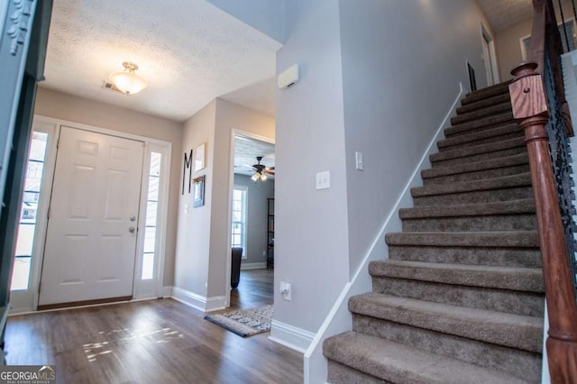 foyer featuring a textured ceiling, wood finished floors, visible vents, baseboards, and stairs