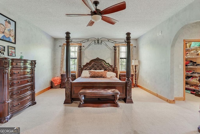 carpeted bedroom with arched walkways, a walk in closet, multiple windows, and a textured ceiling