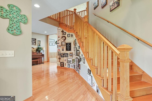 stairway with a high ceiling, wood-type flooring, recessed lighting, and a healthy amount of sunlight