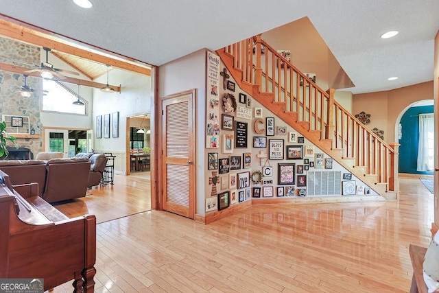 interior space featuring arched walkways, a stone fireplace, wood finished floors, a ceiling fan, and stairs