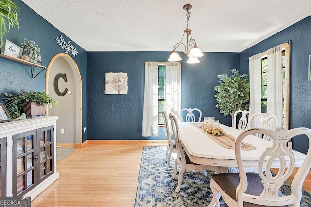 dining space featuring arched walkways, a textured ceiling, wood finished floors, baseboards, and an inviting chandelier